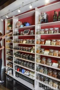 Spices in glass jars on a wooden shelf in a kitchen.