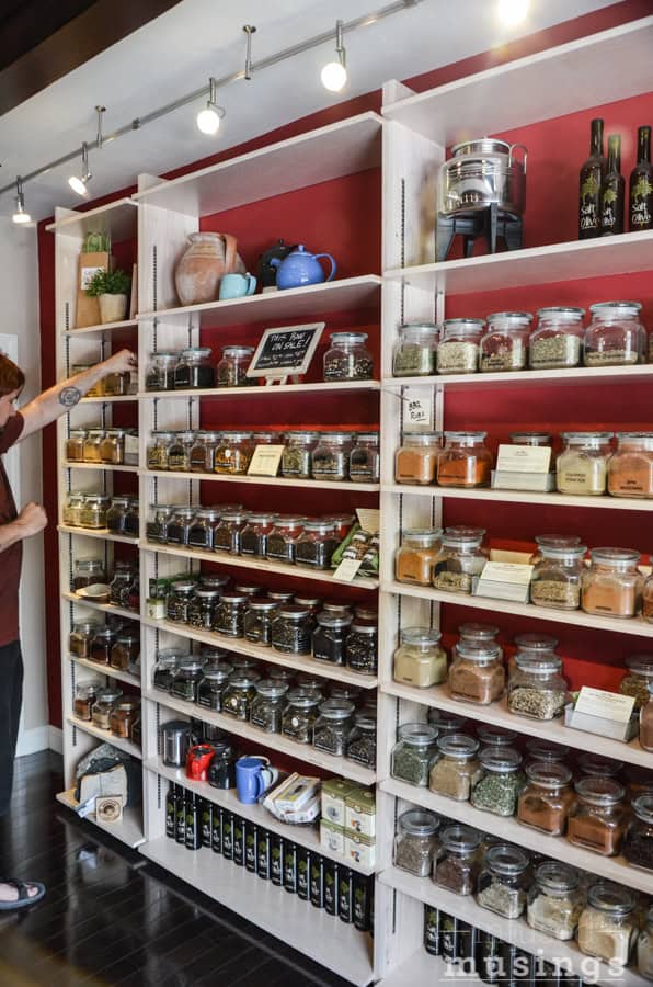 Spices in glass jars on a wooden shelf in a kitchen.