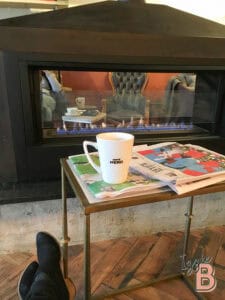 Warm fireplace with newspaper and coffee mug in cozy setting.