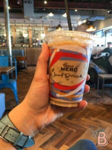 Close-up of iced coffee drink with colorful label and straw in a cozy café setting.