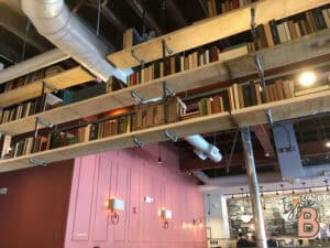 Brightly lit industrial-style bookstore interior with floating wooden shelves filled with books.