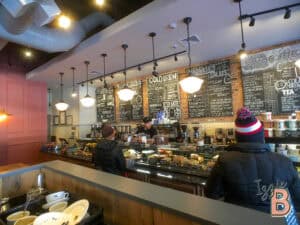 Cozy café scene with modern decor, barista preparing drinks, and customers ordering.