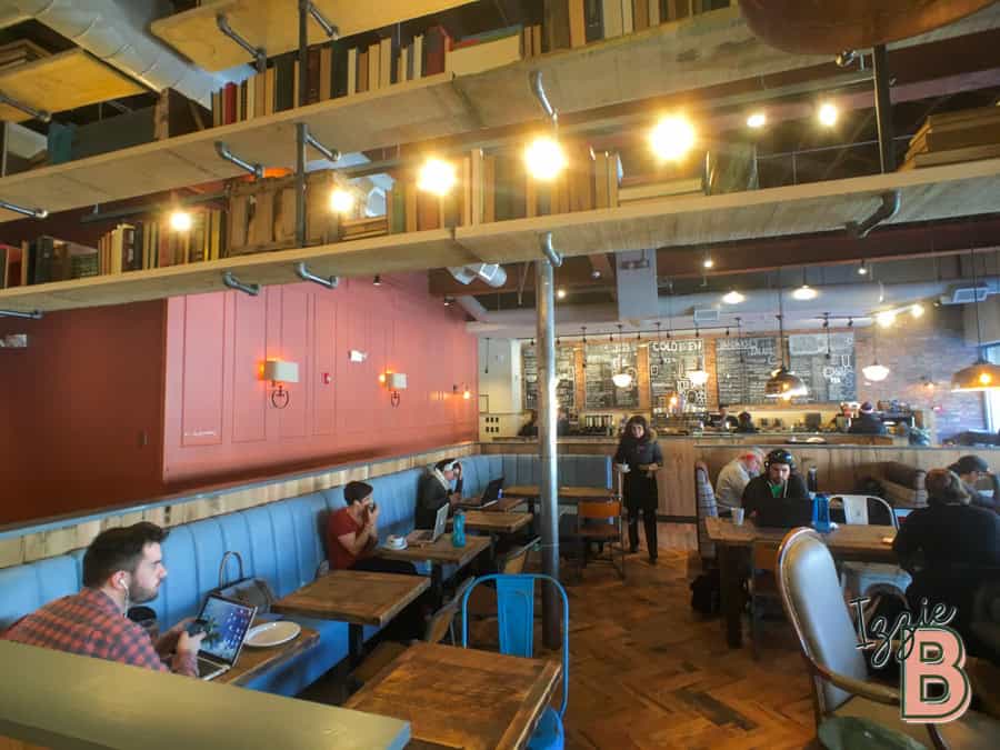 Brightly lit modern café with wooden accents, bookshelves, and comfortable seating for remote work and socializing.