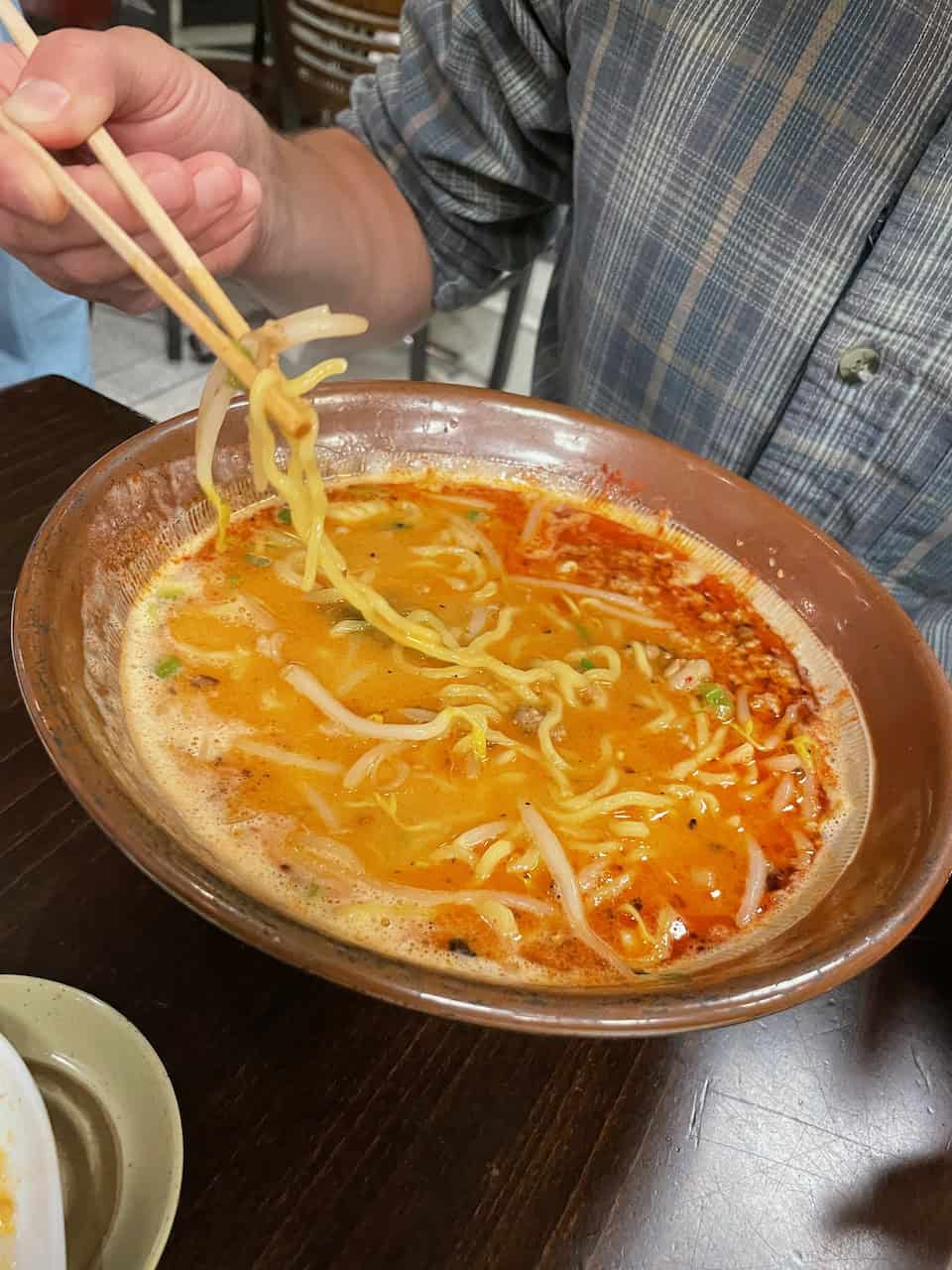 Close-up of a bowl of spicy ramen with noodles, broth, and vegetables served in a restaurant.