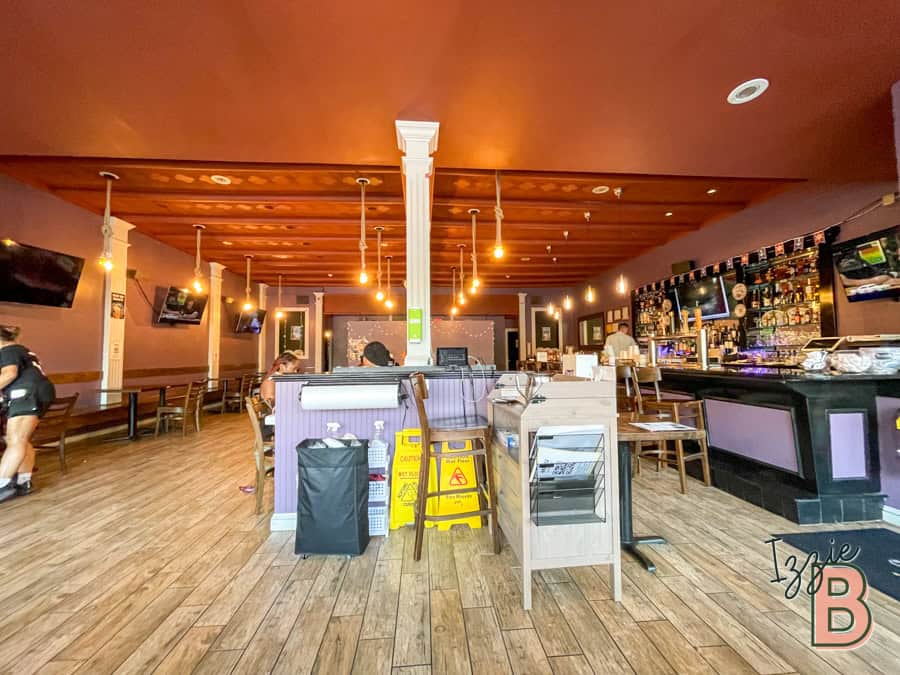 Bright bar scene with wooden floors and TV monitors, lively atmosphere, and seating area.