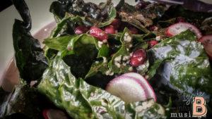 Vibrant kale salad with pomegranate seeds and radish slices, perfect for holiday celebrations and healthy eating.