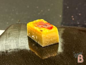 Delicious cheesecake cube with caramelized top served on black plate. Perfect treat for cheesecake lovers.