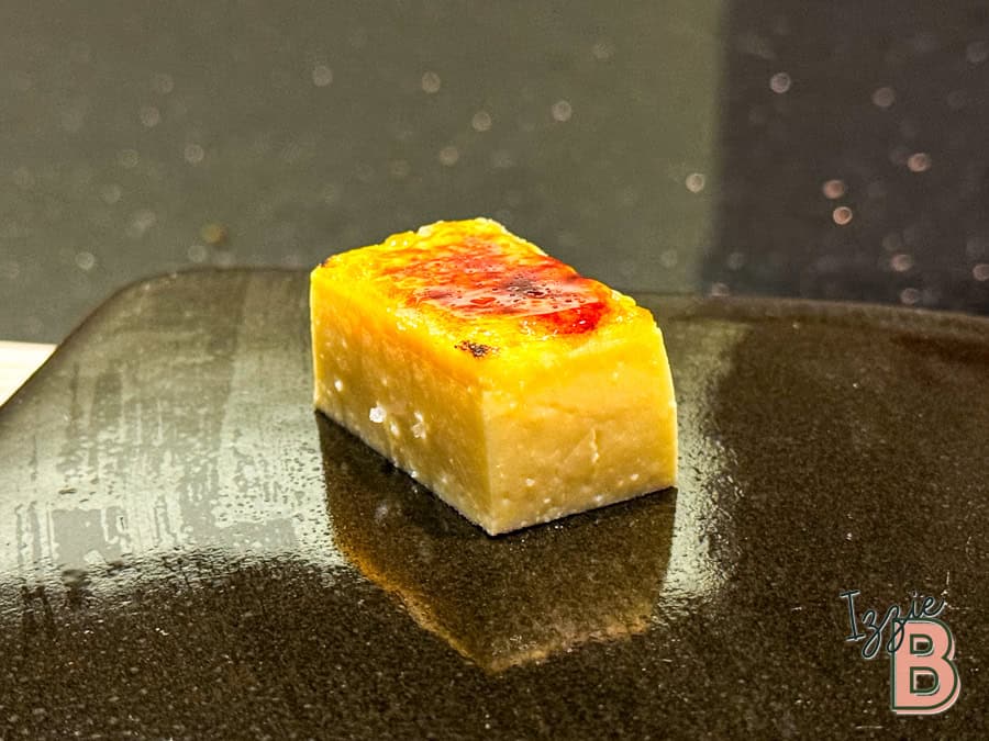 Delicious cheesecake cube with caramelized top served on black plate. Perfect treat for cheesecake lovers.