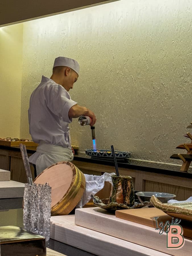 Chef using blowtorch on dish in restaurant kitchen.