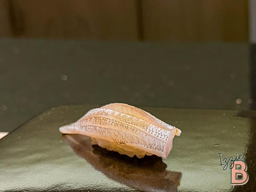 Close-up of a delicate sushi piece with detailed fish topping on a shiny surface.