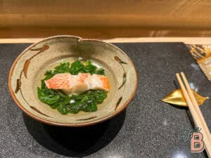 Japanese crab sashimi served with fresh greens in a rustic ceramic bowl.
