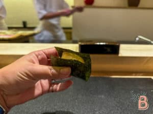 Delicious sushi hand roll with lemon, seaweed wrap, and fresh ingredients at a sushi bar.