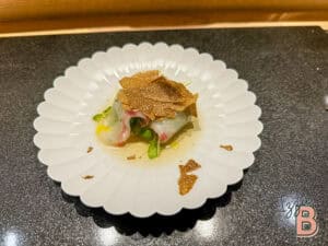 Gourmet dish with truffles, seafood, and greens served on a white scalloped plate, perfect for fine dining.