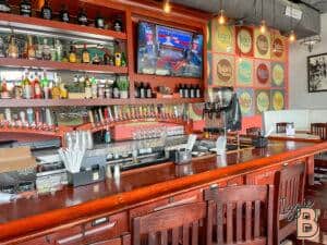 Bar with various liquor bottles, beer taps, and a TV in a lively restaurant setting.