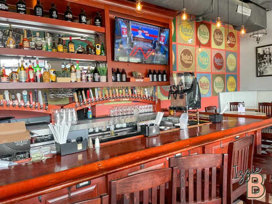 Bar with various liquor bottles, beer taps, and a TV in a lively restaurant setting.