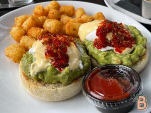 Delicious avocado eggs benedict served with crispy tater tots and salsa, perfect for brunch or breakfast.