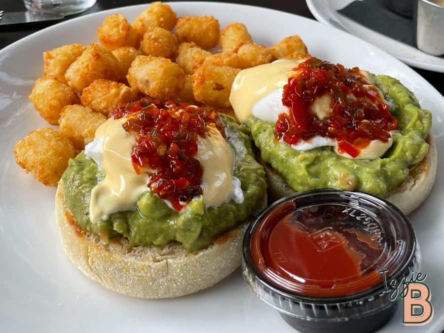 Delicious avocado eggs benedict served with crispy tater tots and salsa, perfect for brunch or breakfast.