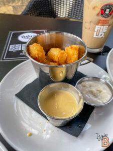 Close-up of crispy chicken bites served with dipping sauces and iced coffee on a restaurant plate.