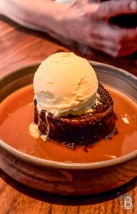 Delicious dessert featuring warm toffee pudding with vanilla ice cream, drizzled with caramel sauce, served in a rustic bowl.